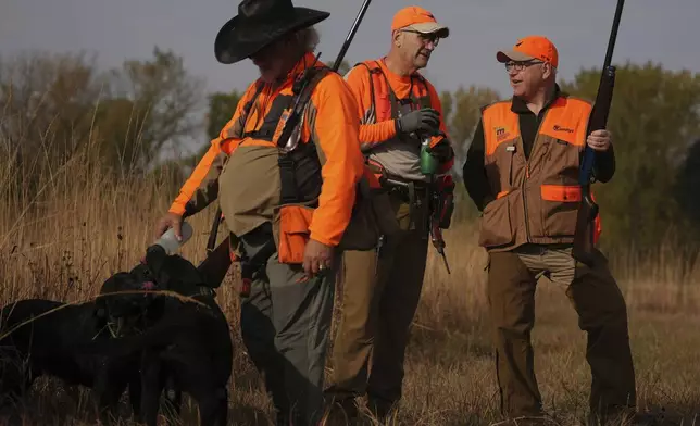 Tim Walz, Minnesota governor and Democratic vice presidential candidate, talks with Matt Kucharski, as Scott Rall gives water to his three hunting dogs, during the annual Minnesota Governor's Pheasant Hunting Opener near Sleepy Eye, Minn., Saturday, Oct. 12, 2024. (Anthony Souffle/Star Tribune via AP)