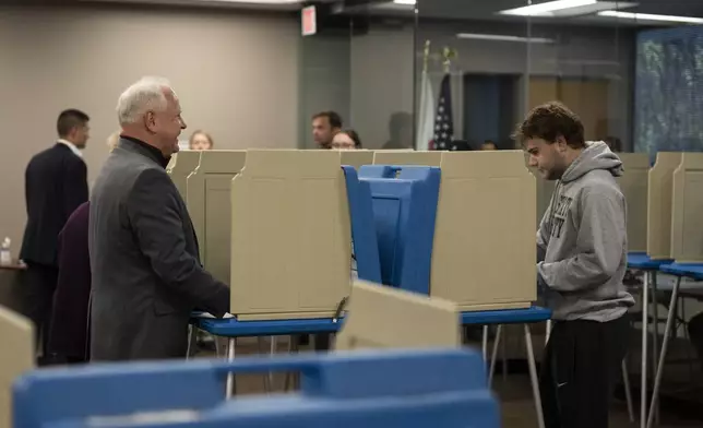 Minnesota Governor and Vice Presidential candidate Tim Walz, left, chats with his son, Gus Walz, a first time voter, as they cast their ballots during early voting at Ramsey County Elections in St. Paul, Minn., on Wednesday, October 23, 2024. (Renée Jones Schneider/Star Tribune via AP)