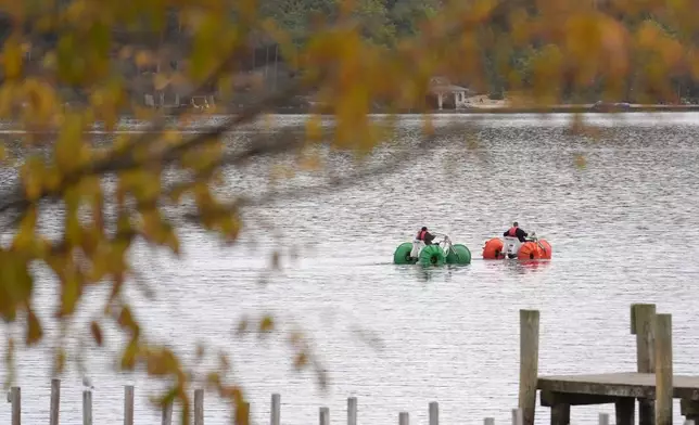 Leaves on trees display bright colors as people using water craft float on Meredith Bay, in Meredith, N.H., Wednesday, Oct. 2, 2024. (AP Photo/Steven Senne)