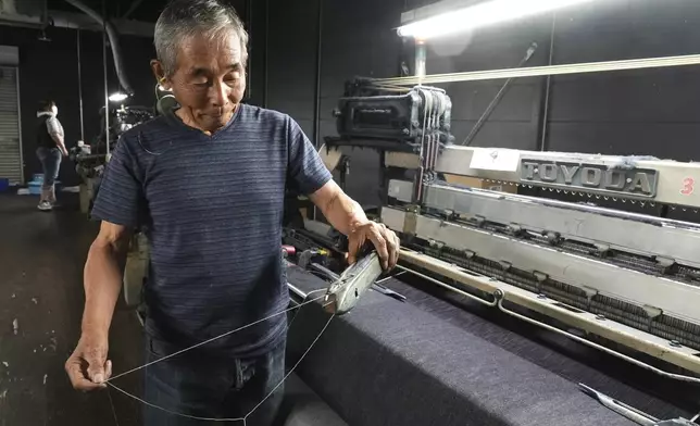 Shigeru Uchida, a weaver at Momotaro Jeans, holds a wooden shuttle next to a vintage loom machine in Kojima, Okayama prefecture, Japan, on Sept. 4, 2024. (AP Photo/Ayaka McGill)