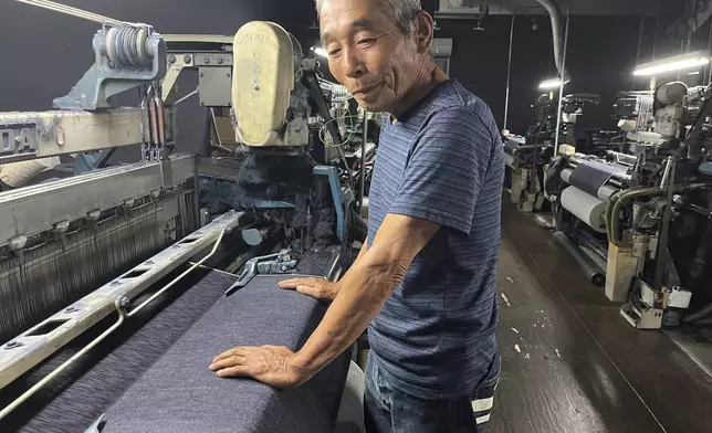 Weaving craftsman Shigeru Uchida examines the evenness of the fabric being woven by the old power looms at Momotaro Jeans in Kojima, Okayama prefecture, Japan, on Sept. 4, 2024. (AP Photo/Yuri Kageyama)