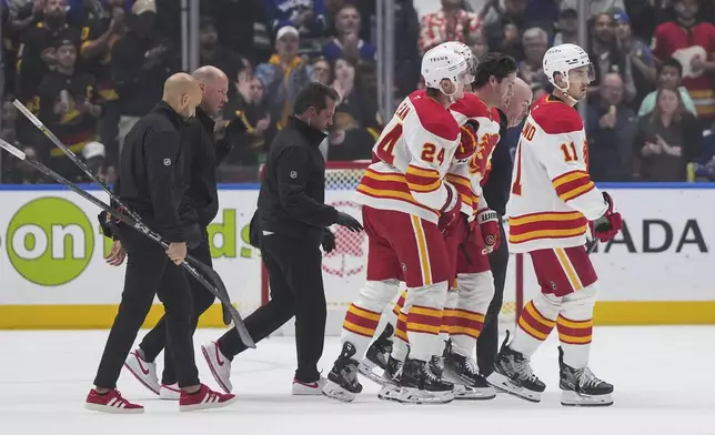 Calgary Flames' Kevin Rooney, second right, is helped off the ice by Jake Bean (24) as Mikael Backlund (11) skates with them after Rooney was checked into the boards during the first period of an NHL hockey game against the Vancouver Canucks, in Vancouver, on Wednesday, Oct. 9, 2024. (Darryl Dyck/The Canadian Press via AP)