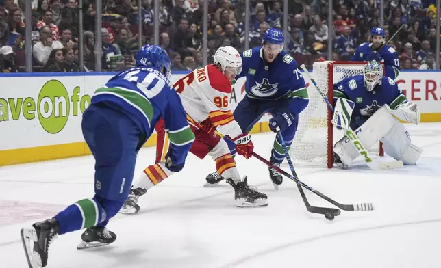 Calgary Flames' Andrei Kuzmenko (96) has the puck knocked off his stick by Vancouver Canucks' Vincent Desharnais (73) as goalie Arturs Silovs (31) and Elias Pettersson, front left, watch during the second period of an NHL hockey game in Vancouver, on Wednesday, Oct. 9, 2024. (Darryl Dyck/The Canadian Press via AP)