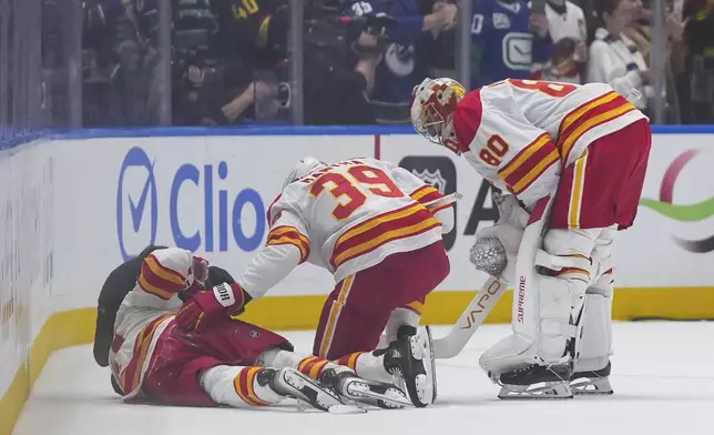 Calgary Flames' Anthony Mantha (39) and goalie Dan Vladar (80) check on teammate Kevin Rooney as he receives medical attention after being checked into the boards during the first period of an NHL hockey game in Vancouver, British Columbia, Wednesday, Oct. 9, 2024. (Darryl Dyck/The Canadian Press via AP)