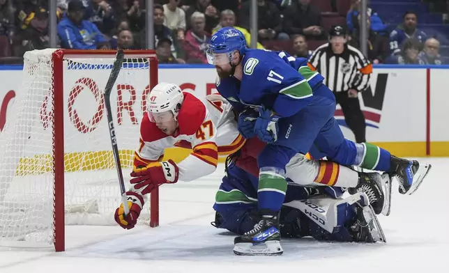 Calgary Flames' Connor Zary (47) celebrates his winning goal against Vancouver Canucks goalie Arturs Silovs, back, while being checked by Filip Hronek (17) during overtime of an NHL hockey game in Vancouver, British Columbia, Wednesday, Oct. 9, 2024. (Darryl Dyck/The Canadian Press via AP)