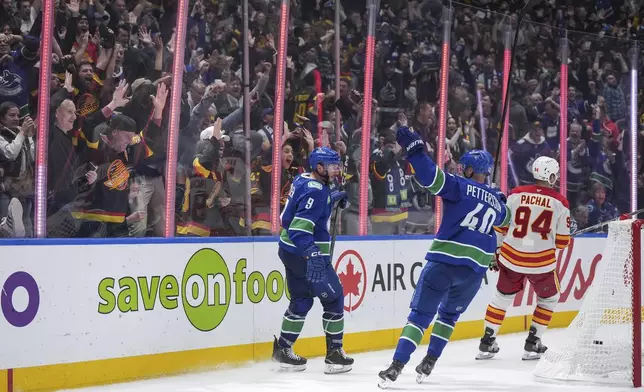 Vancouver Canucks' J.T. Miller (9) and Elias Pettersson (40) celebrate Miller's goal as Calgary Flames' Brayden Pachal (94) skates past during the third period of an NHL hockey game in Vancouver, British Columbia, Wednesday, Oct. 9, 2024. (Darryl Dyck/The Canadian Press via AP)