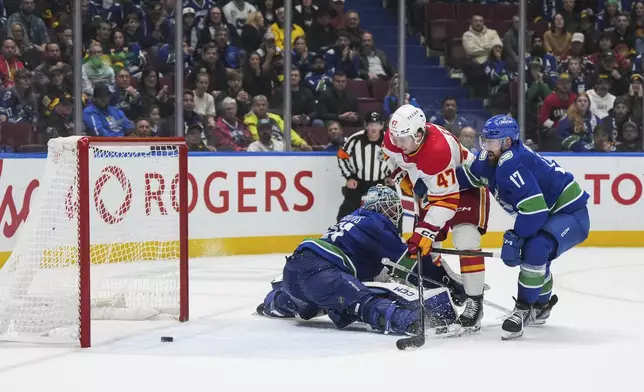 Calgary Flames' Connor Zary (47) scores the winning goal against Vancouver Canucks goalie Arturs Silovs, left, as Filip Hronek (17) defends during overtime of an NHL hockey game in Vancouver, British Columbia, Wednesday, Oct. 9, 2024. (Darryl Dyck/The Canadian Press via AP)