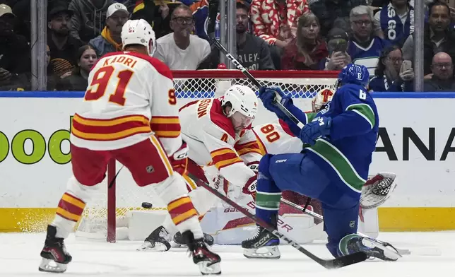 Vancouver Canucks' Brock Boeser, front right, scores against Calgary Flames goalie Dan Vladar (80) as Rasmus Andersson (4) defends and Nazem Kadri (91) watches during the first period of an NHL hockey game, Wednesday, Oct. 9, 2024 in Vancouver, British Columbia. (Darryl Dyck/Canadian Press via AP)