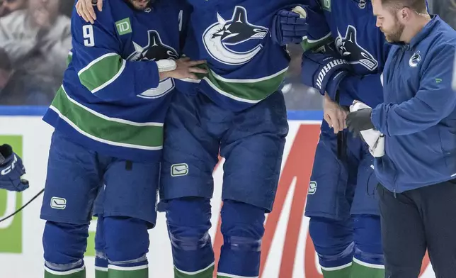 Vancouver Canucks' Tyler Myers (57) is helped off the ice by J.T. Miller (9) and Derek Forbort (27) after a collision on the ice during the first period of an NHL hockey game against the Philadelphia Flyers in Vancouver, Friday, Oct. 11, 2024. (Ethan Cairns/The Canadian Press via AP)