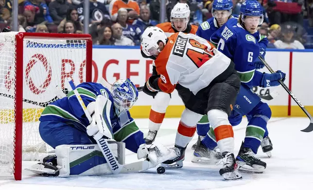 Vancouver Canucks goaltender Kevin Lankinen, left, stops Philadelphia Flyers' Morgan Frost, centre, as Vancouver's Brock Boeser (6) watches during the second period of an NHL hockey game in Vancouver, Friday, Oct. 11, 2024. (Ethan Cairns/The Canadian Press via AP)