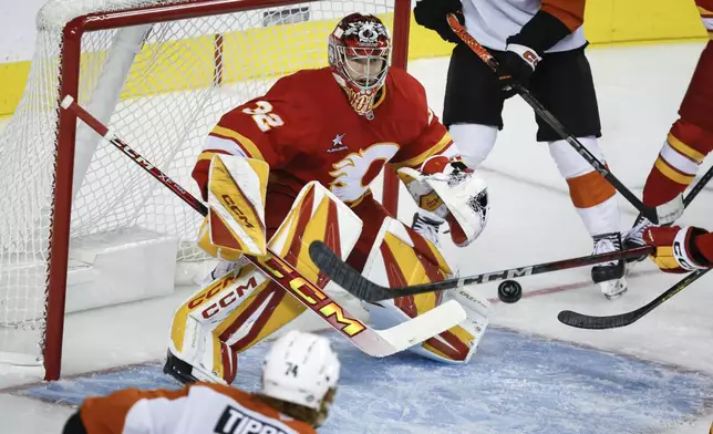 Philadelphia Flyers' Owen Tippett, bottom left, looks on as Calgary Flames goalie Dustin Wolf, center, tracks the puck during the second period of an NHL hockey game in Calgary, Alberta, Saturday, Oct. 12, 2024. (Jeff McIntosh/The Canadian Press via AP)