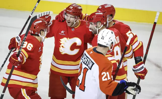 Philadelphia Flyers' Scott Laughton (21) skates past as Calgary Flames' Jonathan Huberdeau, second left, celebrates his goal with teammates during the first period of an NHL hockey game in Calgary Alberta, Saturday, Oct. 12, 2024. (Jeff McIntosh/The Canadian Press via AP)