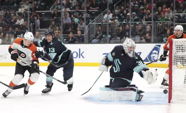 Seattle Kraken goaltender Philipp Grubauer (31) makes a save as left wing Brandon Tanev (13) defends against Philadelphia Flyers right wing Matvei Michkov, left, during the first period of an NHL hockey game Thursday, Oct. 17, 2024, in Seattle. (AP Photo/Jason Redmond)