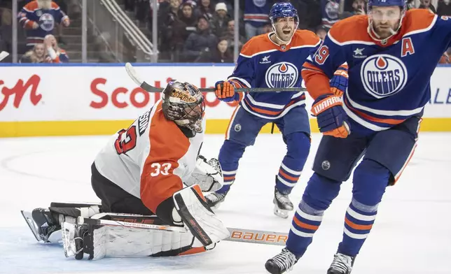 Edmonton Oilers' Evan Bouchard, center, and Leon Draisaitl, right, celebrate Draisaitl's game-winning goal on Philadelphia Flyers goalie Samuel Ersson (33) during overtime of an NHL hockey game in Edmonton, Alberta, Tuesday, Oct. 15, 2024. (Amber Bracken/The Canadian Press via AP)