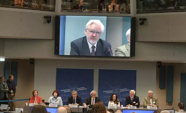 Wikileaks founder Julian Assange is seen an a giant screen as he assesses the Council of Europe while his wife Stella Assange sits next to him, in Strasbourg, eastern France, Tuesday, Oct. 1, 2024. (AP Photo/Pascal Bastien)
