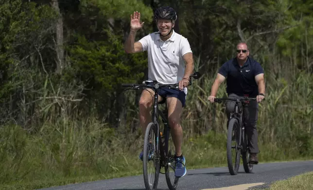 FILE - President Joe Biden waves to a cheering crowd as he rides his bike followed by a Secret Service agent at Gordons Pond in Rehoboth Beach, Del., Sunday, Aug. 11, 2024. (AP Photo/Manuel Balce Ceneta, File)