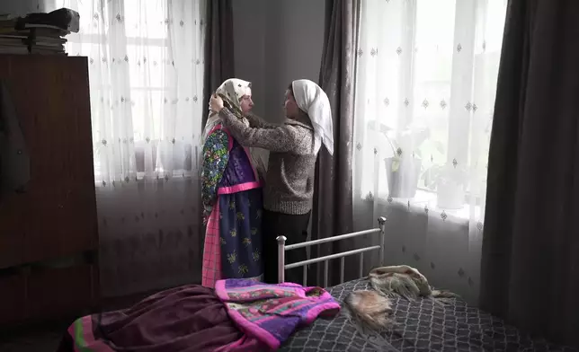 Daria Strukova, right, helps her sister Nina Strukova, left, put on a traditional Doukhobor dress in the remote mountain village of Orlovka, Georgia, Sunday, May 5, 2024. (AP Photo/Kostya Manenkov)