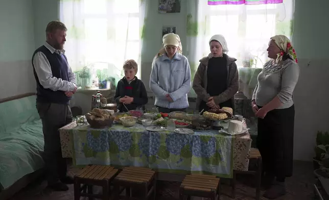 Yuri Strukov, left, his son Ilya, daughters Nina and Daria, and his wife Svetlana Svetlishcheva, right, pray before a meal in their house in the remote mountain village of Orlovka, Georgia, Saturday, May 5, 2024. (AP Photo/Kostya Manenkov)