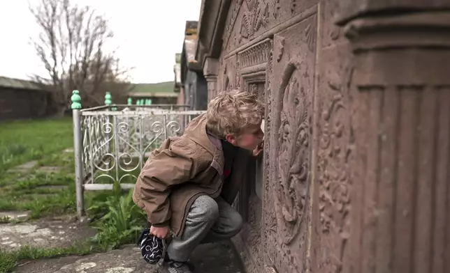 Ilya Strukov, 10, kisses a tombstone on a grave of his Doukhobor ancestors at a cemetery outside of the remote mountain village of Orlovka, Georgia, Sunday, May 5, 2024. (AP Photo/Kostya Manenkov)