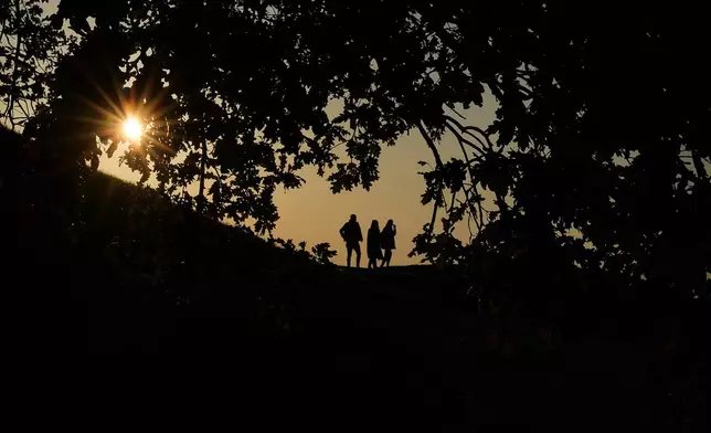 People stroll through the Olympic park as the sun sets in Munich, Germany, Tuesday, Oct. 29, 2024. (AP Photo/Matthias Schrader)