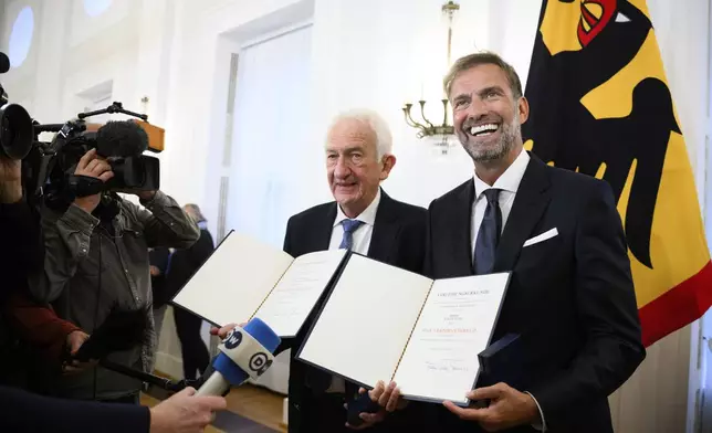Johann Georg Goldammer and Jurgen Klopp stand in Bellevue Palace after receiving the Order of Merit of the Federal Republic of Germany and show their certificates as Federal President Steinmeier honors 28 citizens on the Day of German Unity, in Berlin, Tuesday, Oct. 1, 2024. (Bernd von Jutrczenka/dpa via AP)