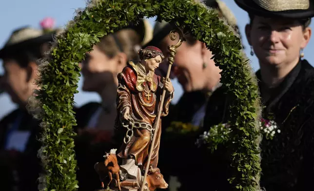 A woman in traditional costume of the region sits behind a St. Leonhard statue during the the Leonhardi pilgrimage in Warngau near Munich, Germany, Sunday, Oct. 27, 2024. The annual pilgrimage honors St. Leonhard, patron saint of the highland farmers for horses and livestock. (AP Photo/Matthias Schrader)