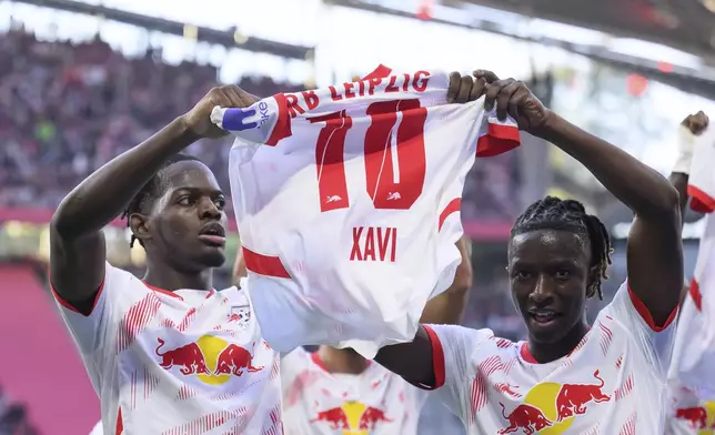 Leipzig's Castello Lukeba, left, and Amadou Haidara hold up a jersey of the injured Xavi Simons during the German Bundesliga soccer match between RB Leipzig and SC Freiburg at the Red Bull Arena in Leipzig, Germany, Saturday, Oct. 26, 2024. (Hendrik Schmidt/dpa via AP)