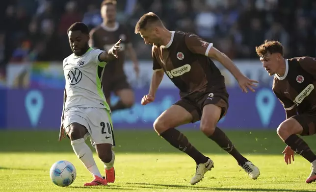 From left, VfL Wolfsburg, Wolfsburg's Ridle Baku and St. Pauli's Karol Mets and Philipp Treu fight for the bal during the German Bundesliga soccer match between VfL Wolfsburg and FC St. Pauli in Hamburg, Germany, Saturday, Oct. 26, 2024. (Marcus Brandt/dpa via AP)