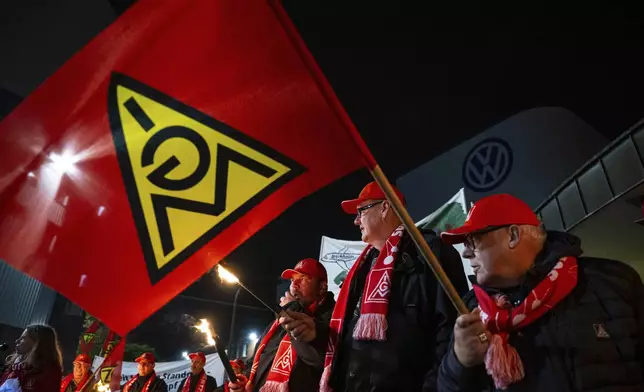 Volkswagen employees stand with torches in front of the VW plant in Osnabruck, Germany, Tuesday, Oct. 29, 2024. (Guido Kirchner/dpa via AP)