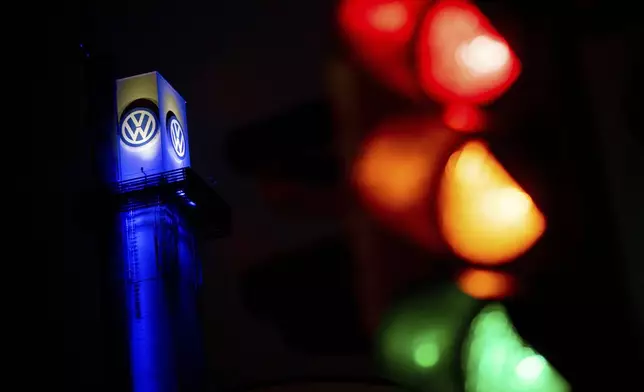 A traffic light shines in front of a Volkswagen logo at the Volkswagen plant in Osnabruck, Germany, Tuesday, Oct. 29, 2024. (Hauke-Christian Dittrich/dpa via AP)
