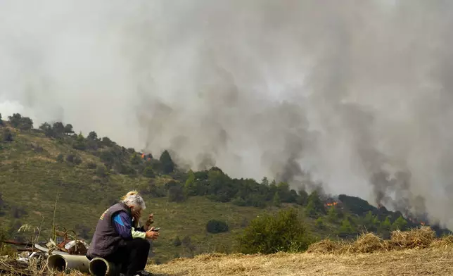 People react as flames burn a forest in Sofiana village, about 142 kilometers (88 miles) west of Athens, Greece, on Tuesday, Oct. 1, 2024 while hundreds of firefighters and volunteers for a third day battled a large wildfire in the mountains of Corinthia in the Peloponnese region. (AP Photo/Petros Giannakouris)