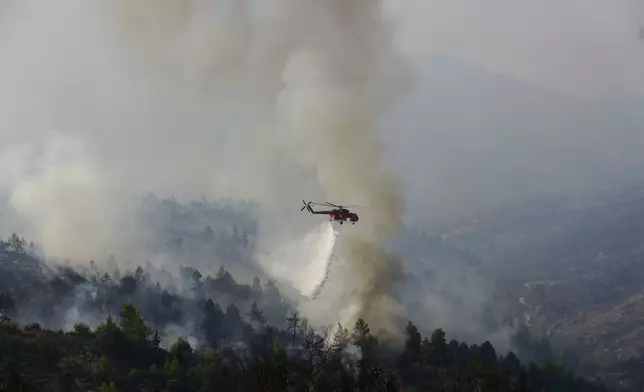 A helicopter drops water on flames during a third day of a wildfire, in Sofiana village, about 142 kilometers (88 miles) west of Athens, Greece, on Tuesday, Oct. 1, 2024. (AP Photo/Petros Giannakouris)
