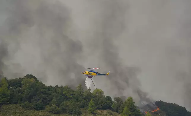A helicopter drops water on flames in Sofiana village, about 142 kilometers (88 miles) west of Athens, Greece, on Tuesday, Oct. 1, 2024 as hundreds of firefighters and volunteers for a third day battled a large wildfire in the mountains of Corinthia in the Peloponnese region. (AP Photo/Petros Giannakouris)