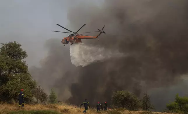A helicopter drops water on flames during a third day of a wildfire, in Sofiana village, about 142 kilometers (88 miles) west of Athens, Greece, on Tuesday, Oct. 1, 2024. (AP Photo/Petros Giannakouris)