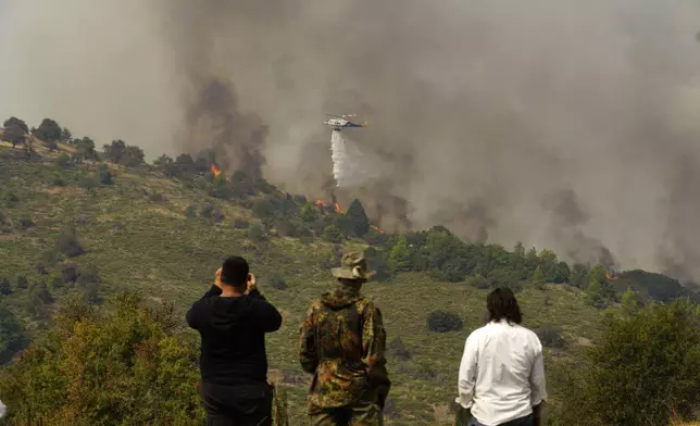 A helicopter drops water on flames in Sofiana village, about 142 kilometers (88 miles) west of Athens, Greece, on Tuesday, Oct. 1, 2024 as hundreds of firefighters and volunteers for a third day battled a large wildfire in the mountains of Corinthia in the Peloponnese region. (AP Photo/Petros Giannakouris)