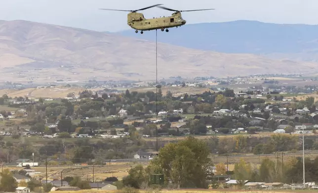 A U.S. Army Chinook helicopter lifts a cargo box out of Vagabond Army Heliport as it heads toward the site of the crashed Navy EA-18G Growler jet on Friday, Oct. 18, 2024, in Yakima, Wash. (Nick Wagner/The Seattle Times via AP)