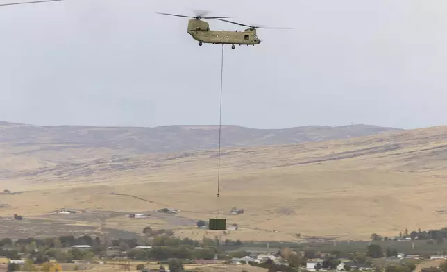 A U.S. Army Chinook helicopter lifts a cargo box out of Vagabond Army Heliport as it heads toward the site of the crashed Navy EA-18G Growler jet on Friday, Oct. 18, 2024, in Yakima, Wash. (Nick Wagner/The Seattle Times via AP)