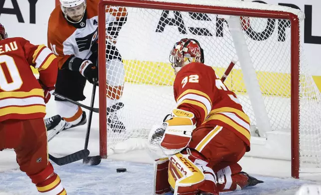 Philadelphia Flyers' Travis Konecny, left, tries to wrap the puck around the net as Calgary Flames goalie Dustin Wolf tries to defend during third period NHL hockey action in Calgary, Alberta, Saturday, Oct. 12, 2024. (Jeff McIntosh/The Canadian Press via AP)