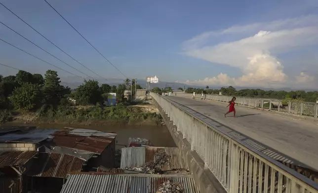 People walk across a bridge in Pont-Sonde, Haiti, Tuesday, Oct. 8, 2024, days after a deadly gang attack in the town. (AP Photo/Odelyn Joseph)