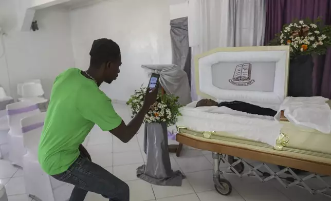 A morgue worker takes a photo of the body of Jean Louis Jeune Gracien, who was killed during an attack by armed gangs, at his funeral in Pont-Sonde, Haiti, Tuesday, Oct. 8, 2024. (AP Photo/Odelyn Joseph)