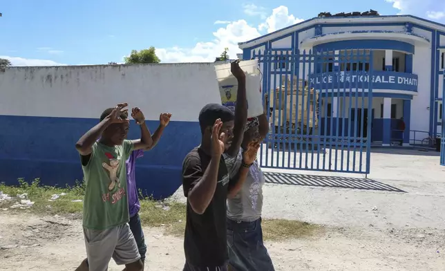 People raise their arms while walking past a police station in Pont-Sonde, Haiti, Monday, Oct. 7, 2024, days after a gang attacked the town. (AP Photo/Odelyn Joseph)