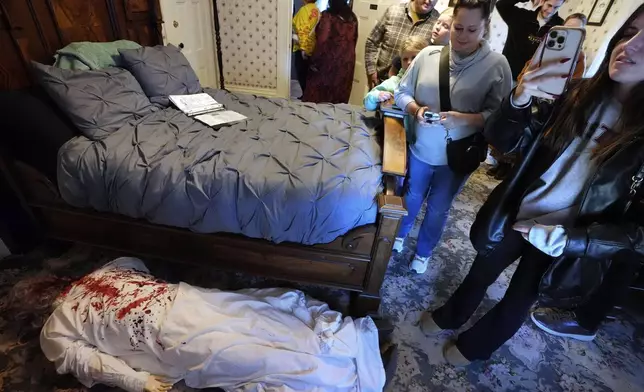 Visitors to the Lizzie Borden House view a mannequin in costume, below left, meant to portray a likeness of the murder scene of Abby Borden, while visiting the site of an 1892 double axe murder, Wednesday, Oct. 16, 2024, in Fall River, Mass. (AP Photo/Steven Senne)