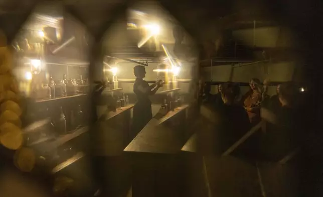 In this image taken through a stained glass window, Natasha Cimmiyotti, left, answers questions while pouring shots of liquor after leading a tour of underground passages on Thursday, Oct. 17, 2024, in Portland, Ore. (AP Photo/Jenny Kane)