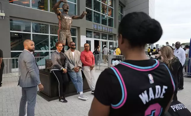 Former Miami Heat player Dwyane Wade, center, poses with fans in front of his statue outside of the Kaseya Center before an NBA basketball game between the Miami Heat and the Detroit Pistons, Monday, Oct. 28, 2024, in Miami. (AP Photo/Lynne Sladky)