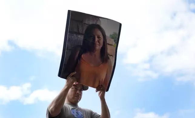 Fernando Ruiz stands silently as he holds a photo of his mother, Lidia Verdugo, who went missing during the flooding caused by Hurricane Helene at Impact Plastics, reminding those attending a press conference she still hadn't been found, in Erwin, Tenn., on Thursday, Oct. 3, 2024. (AP Photo/Jeff Roberson)