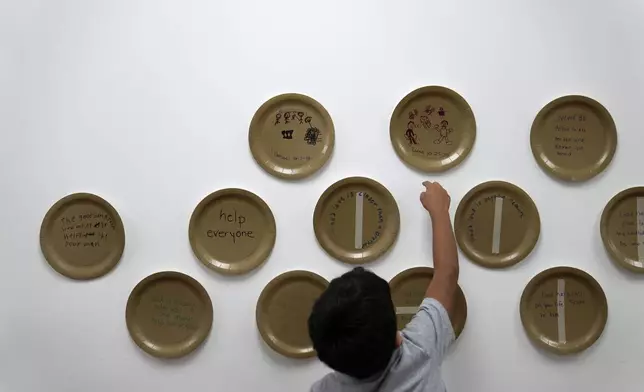 A child reaches for a drawing on a plate he completed inside St. Michael the Archangel Catholic church in Erwin, Tenn., on Friday, Oct. 4, 2024, in the aftermath of Hurricane Helene. (AP Photo/Jeff Roberson)