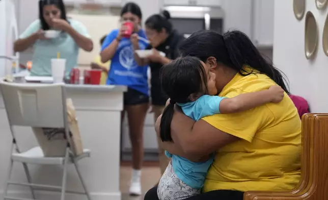 Alexandra Reynoso, right, hugs her little sister, Sofia Reynosa, 5, as others grab a bite to eat in the kitchen of St. Michael the Archangel Catholic church in the aftermath of Hurricane Helene Friday, Oct. 4, 2024, in Erwin, Tenn. (AP Photo/Jeff Roberson)