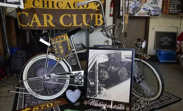 A photo of baby Daniel Marquez, now seven years old, sitting on his late father Alberto's lap inside their 1963 Chevy Impala lowrider car, is displayed with a custom chrome lowrider bike built by Daniel and family friends Saturday, Sept. 14, 2024, at his home in Frankfort, Ill. (AP Photo/Erin Hooley)