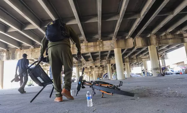 People living in a homeless encampment pick up belongings after Louisiana State police gave instructions for them to move to a different pre-designated location as they perform a sweep in advance of a Taylor Swift concert in New Orleans, Wednesday, Oct. 23, 2024. (AP Photo/Gerald Herbert)