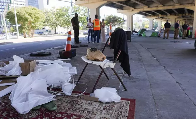 Possessions sit under an overpass as Louisiana State police, right, give instructions to people living in a homeless encampment to move to a different pre-designated location as they perform a sweep in advance of a Taylor Swift concert in New Orleans, Wednesday, Oct. 23, 2024. (AP Photo/Gerald Herbert)